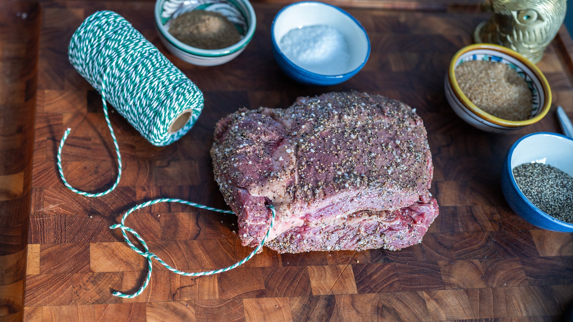 Raw meat on a wooden cutting board with spices and twine