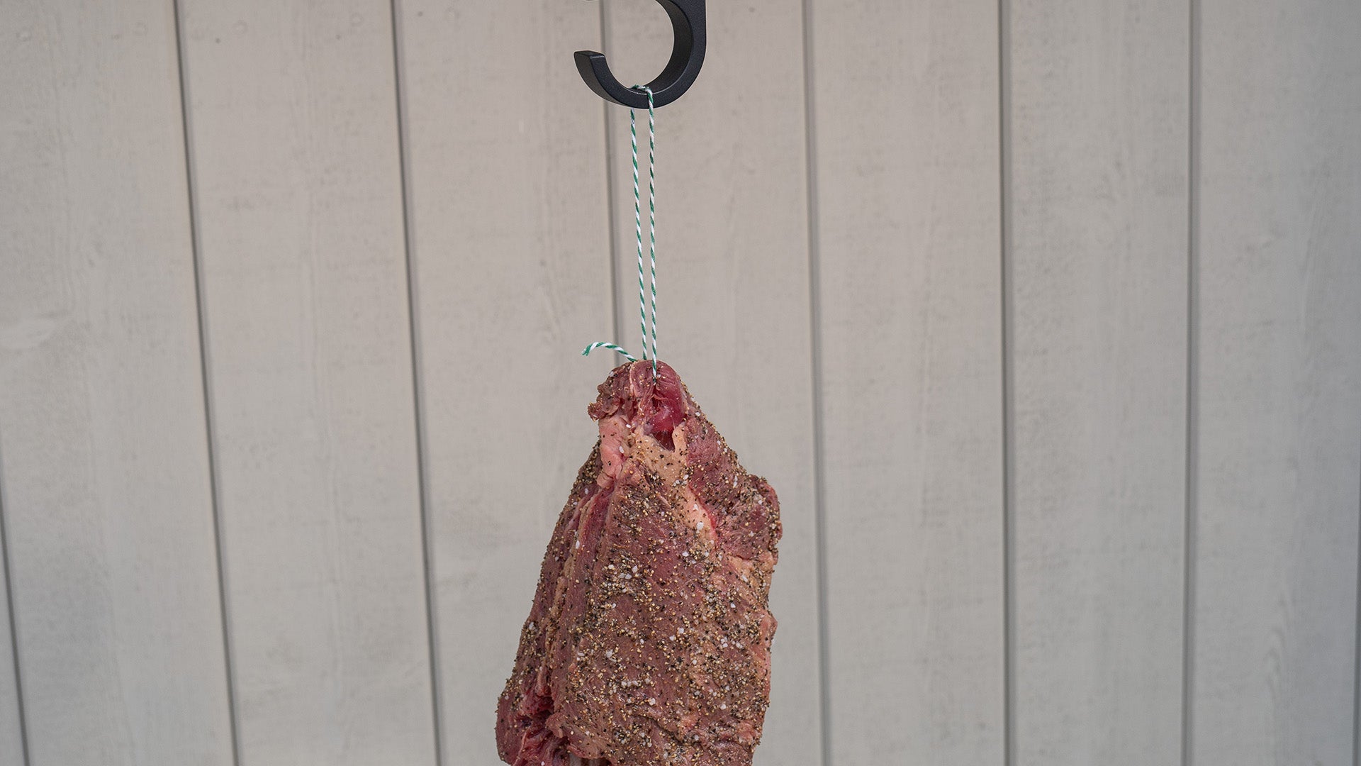 Raw meat hanging from a hook with butcher twine/ meat string, against a plain background
