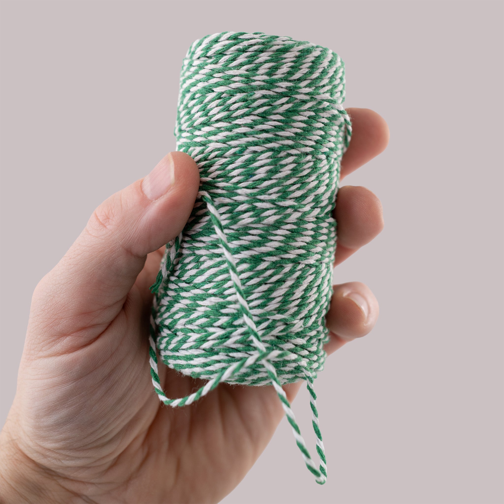 Hand holding a spool of green and white bakers twine against a neutral background