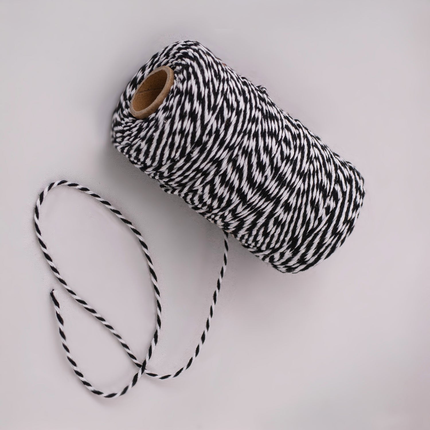 Roll of black and white striped butcher string, butcher twine, meat string, meat twine on a light gray background