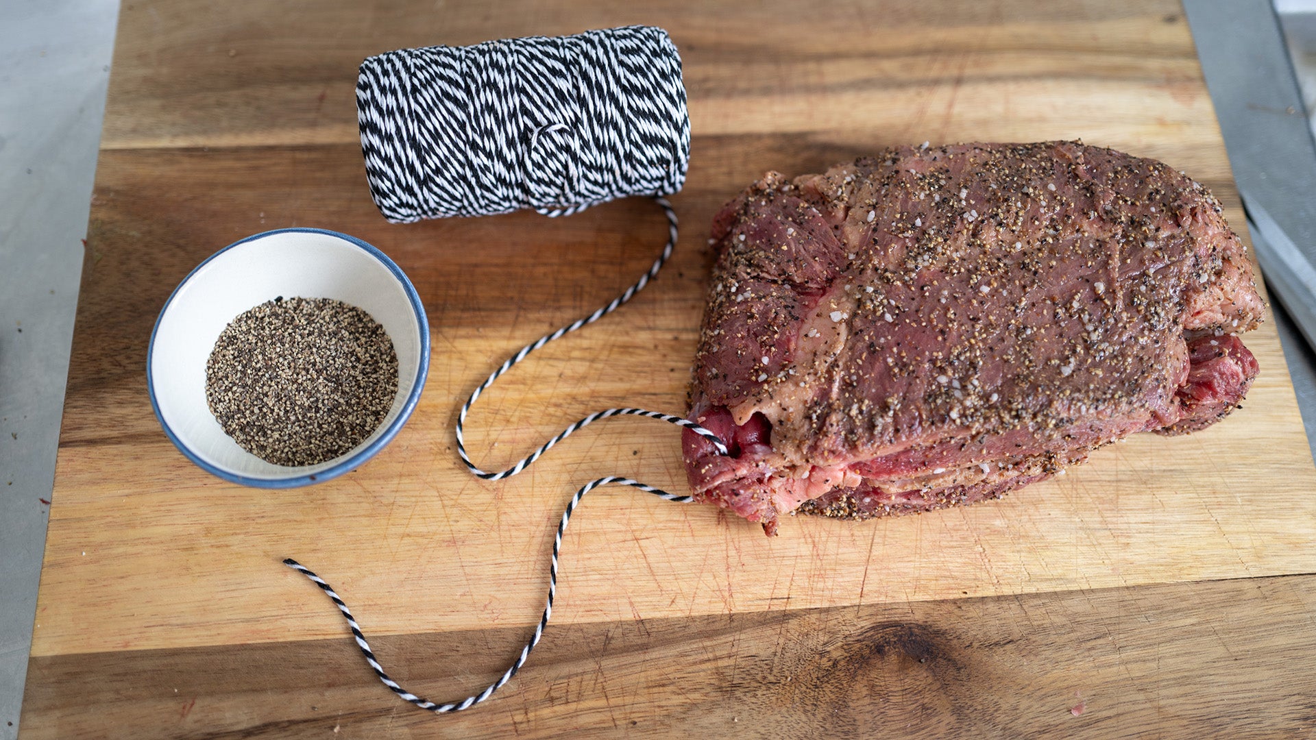 Raw biltong beef on a wooden cutting board with a bowl of spices and butcher twine, meat string