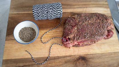 Raw biltong beef on a wooden cutting board with a bowl of spices and butcher twine, meat string