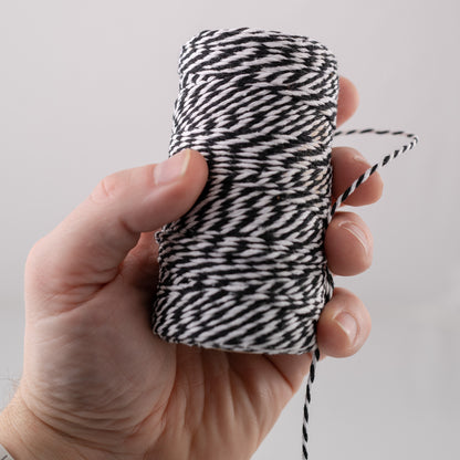 Hand holding a spool of black and white patterned meat string against a light gray background