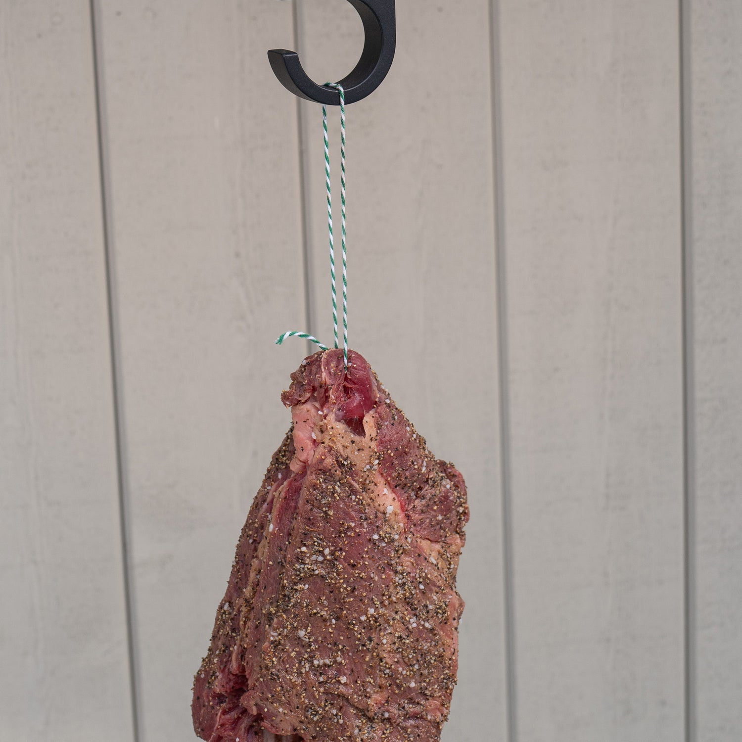 Raw meat hanging from a hook in green and white striped butcher string, butcher twine, meat string, meat twine on a light against a wooden background