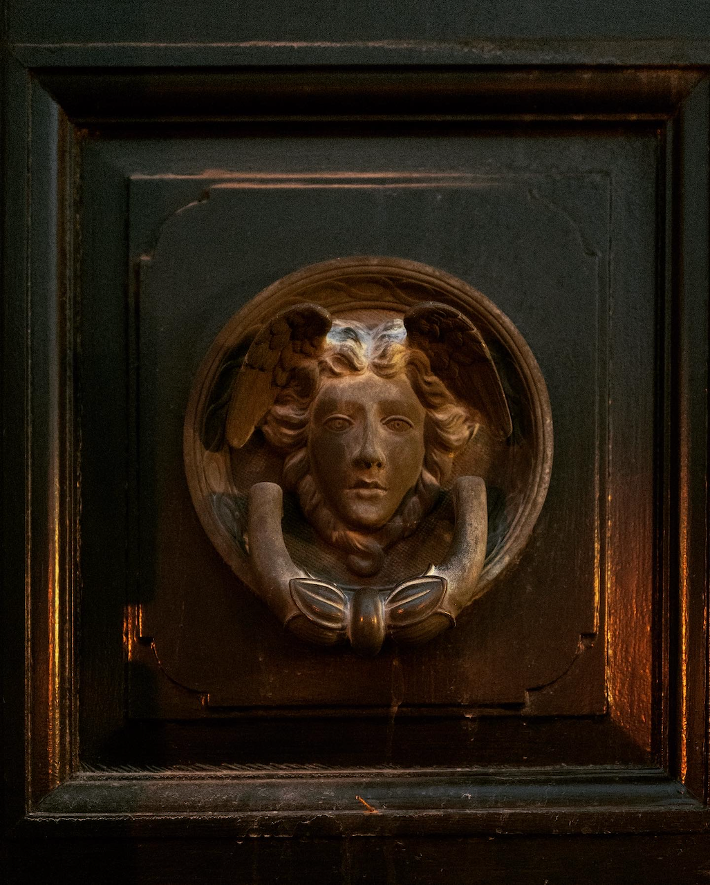 Decorative wall piece with a face and wings on a dark wooden background