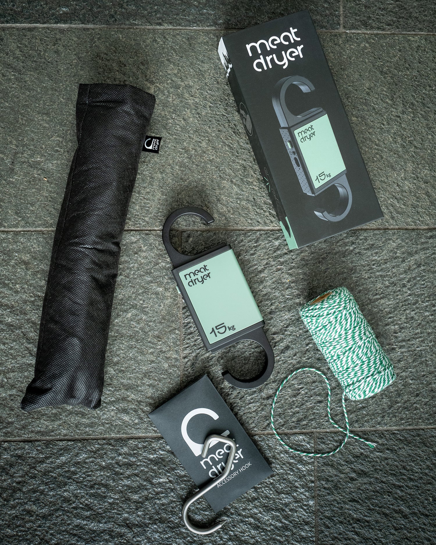 Meat drying equipment including a black insect net, string, and sharp metal meat hook on a stone surface